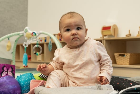A baby sitting on a mat in a room full of toys.