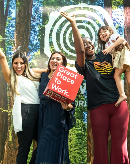 Three women posing in front of a sign that says great places to work.