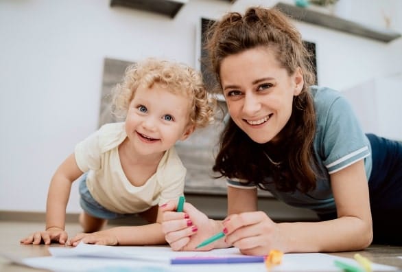 A mother and child playing with crayons on the floor.