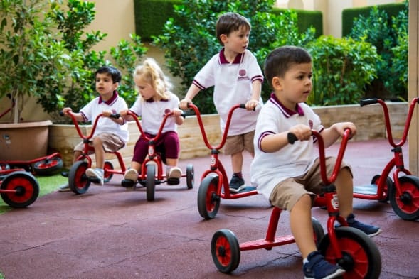 A group of children riding red tricycles in a courtyard.