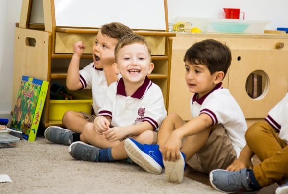 A group of children sitting on the floor in a classroom.