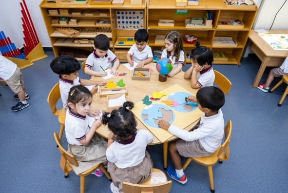 A group of children sitting around a table in a classroom.