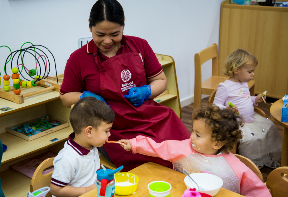 A woman in a red apron is helping children at a table.
